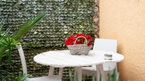 A white wicker table with a basket of red flowers, a white chair, and a textured wall in the background.