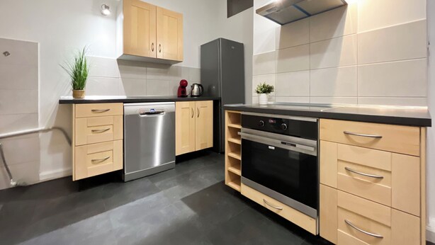 Eine moderne Küche mit Holzschränken, einem Edelstahl-Geschirrspüler, einem eingebauten Backofen und einer schwarzen Dunstabzugshaube.
