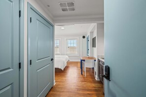 A hallway with a bed, a desk, and a kitchenette.