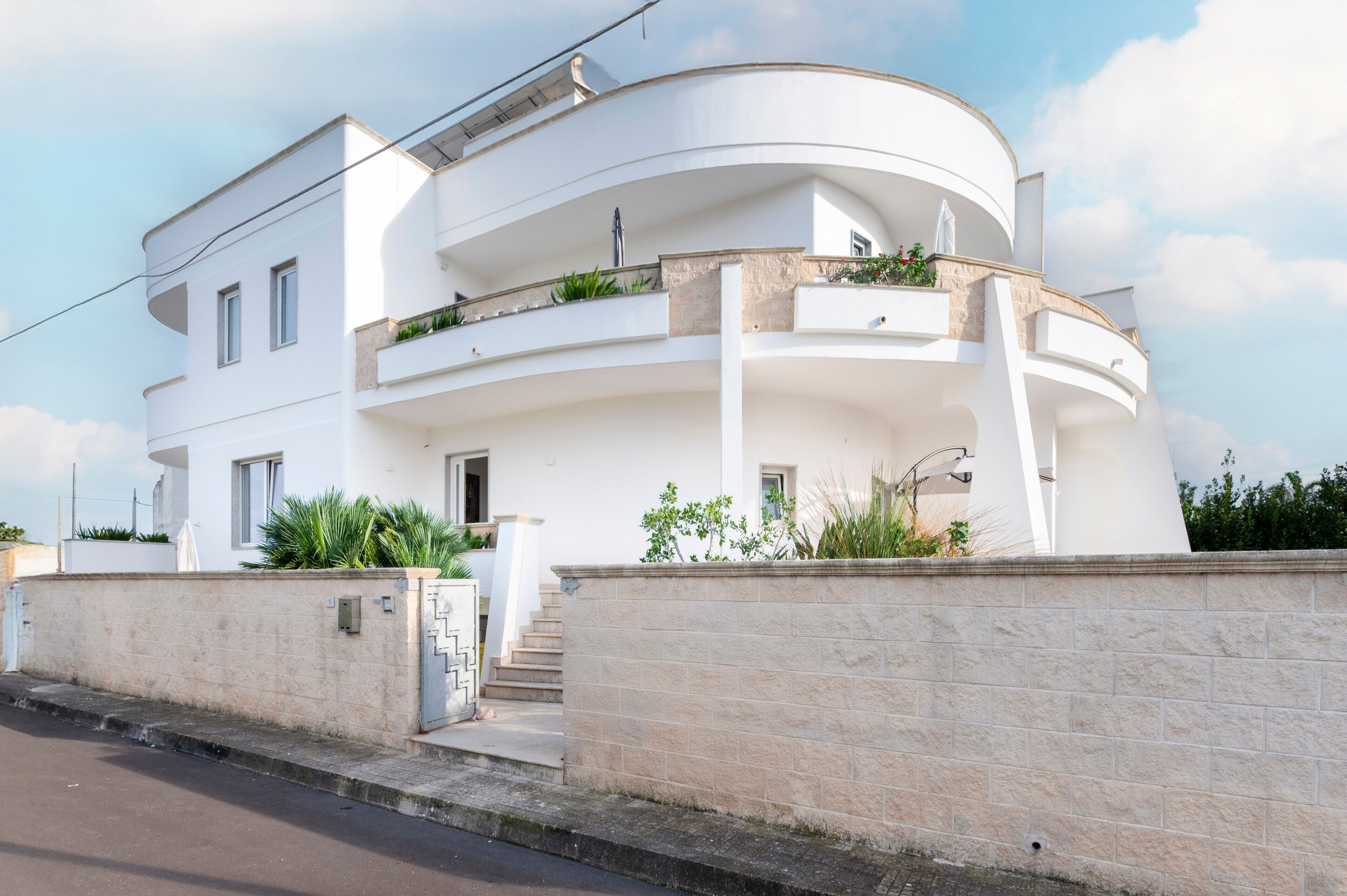 Une maison moderne à deux étages, dotée d’une façade incurvée, d’un balcon agrémenté de plantes et d’un mur en pierre à l’avant.