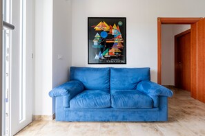 A blue sofa in a room with a geometric art piece on the wall and a wooden door.