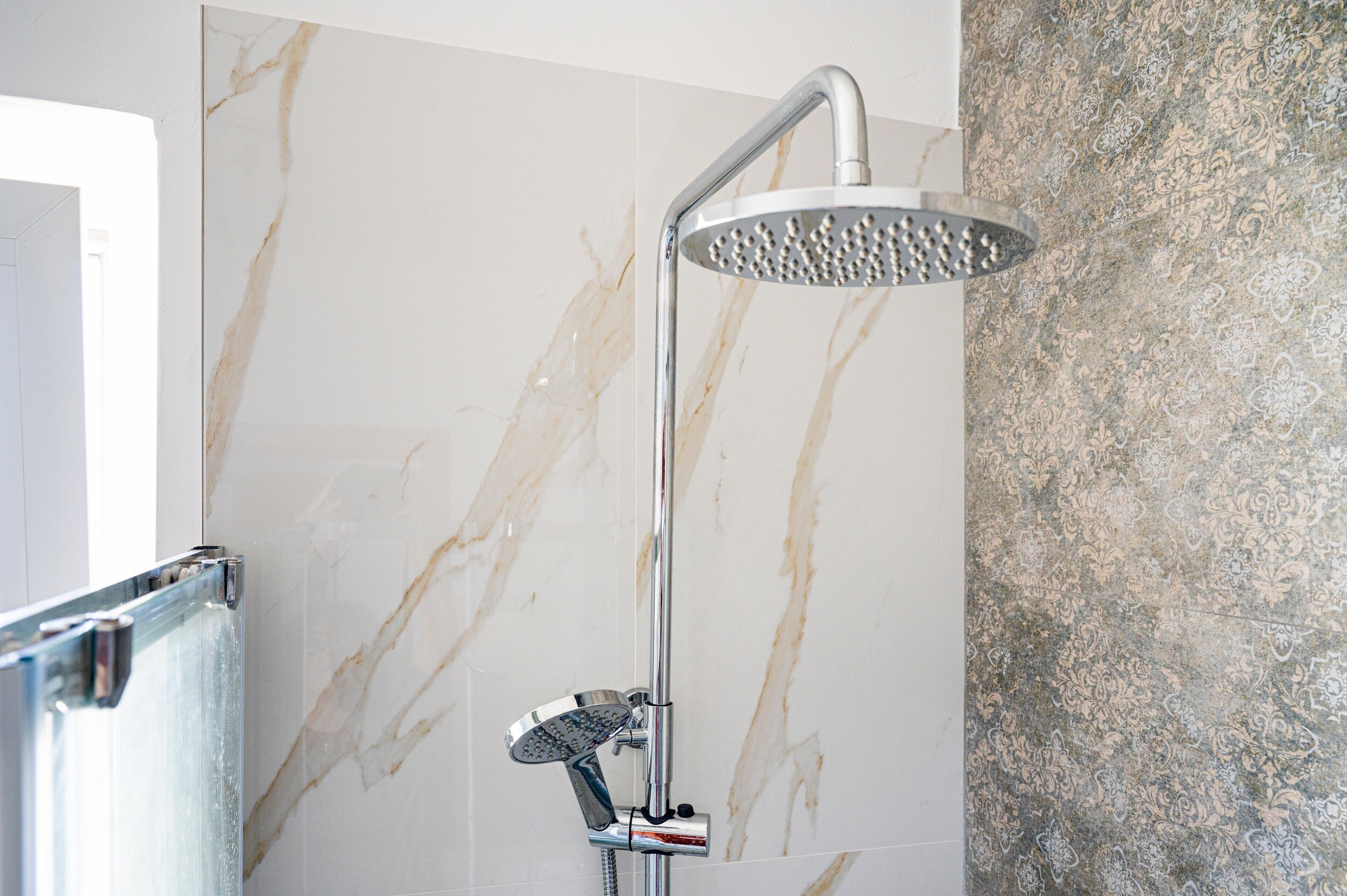 Een moderne douche met een handdouche en een bedieningspaneel aan de muur.