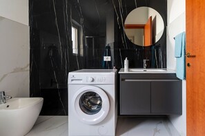 Une salle de bain moderne équipée d’un lave-linge, d’un évier et d’un meuble de rangement.