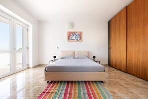 A bedroom with a bed, a colorful striped rug, a painting on the wall, and a wooden wardrobe.