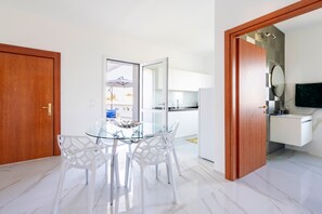 A modern kitchen with white cabinets, a glass dining table, and white chairs.