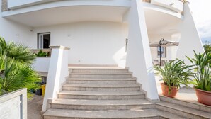 Ein weißes Gebäude mit einem gebogenen Balkon, Steinstufen, die zu einer Tür führen, und Kübelpflanzen.