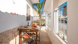 Un balcón exterior estrecho con una mesa dispuesta para dos personas, una botella y un frutero.