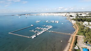 Vista aérea de un puerto deportivo costero con muelles, barcos y una zona de playa.