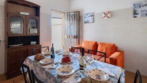 Un área de comedor con una mesa dispuesta para cuatro, un aparador de madera y un sofá anaranjado brillante.