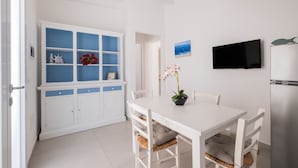 Un espace de salle à manger aux murs blancs, comprenant une table, des chaises, un téléviseur et un meuble avec des portes bleues.