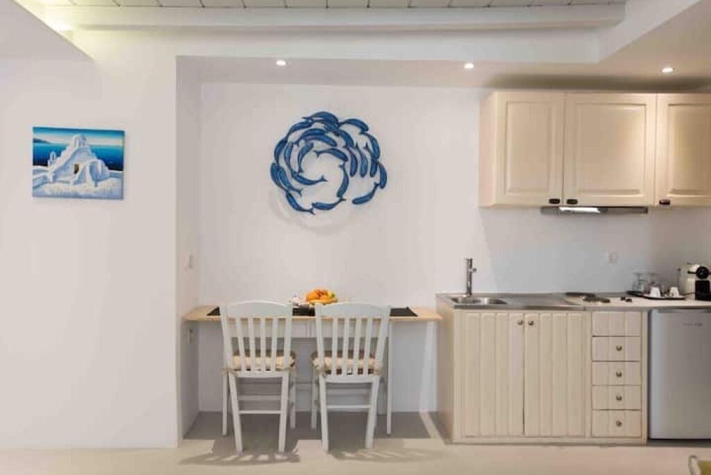 Eine moderne Küche mit weißen Schränken, einem Essbereich mit zwei weißen Stühlen und einer Wand mit einem blauen abstrakten Kunstwerk.