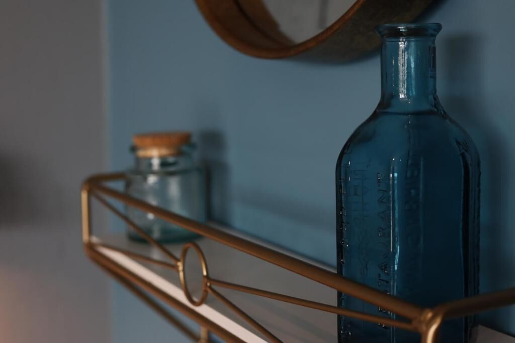 A blue glass bottle on a metal shelf against a blue wall.