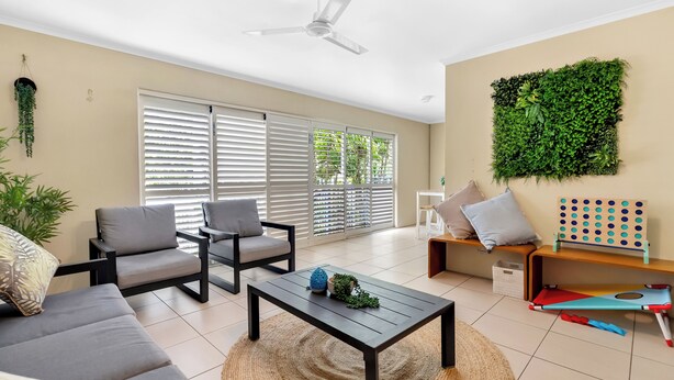Een moderne woonkamer met een bank, stoelen, een salontafel, een plafondventilator, een wandplant en een houten plank met een spel.