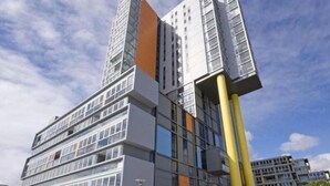 A multi-story building with a modern architectural design, featuring a prominent yellow column and a mix of glass and solid facade elements.