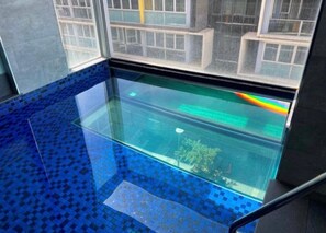 Une piscine à fond de verre offrant une vue sur les bâtiments environnants.