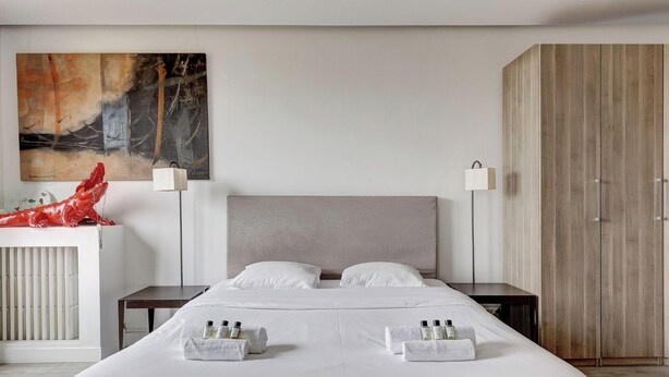 A modern hotel room with a large bed, two bedside tables, a wardrobe, and a large abstract painting on the wall. - Modern 3BR Apartment with Balcony - Pereire (Paris)
