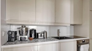 A modern kitchen with white cabinets, a stainless steel sink, a coffee maker, a blender, and a kettle. - Modern 3BR Apartment with Balcony - Pereire (Paris)