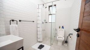 Une salle de bain moderne avec des murs en briques blanches, une douche en verre, un lavabo blanc et des toilettes.
