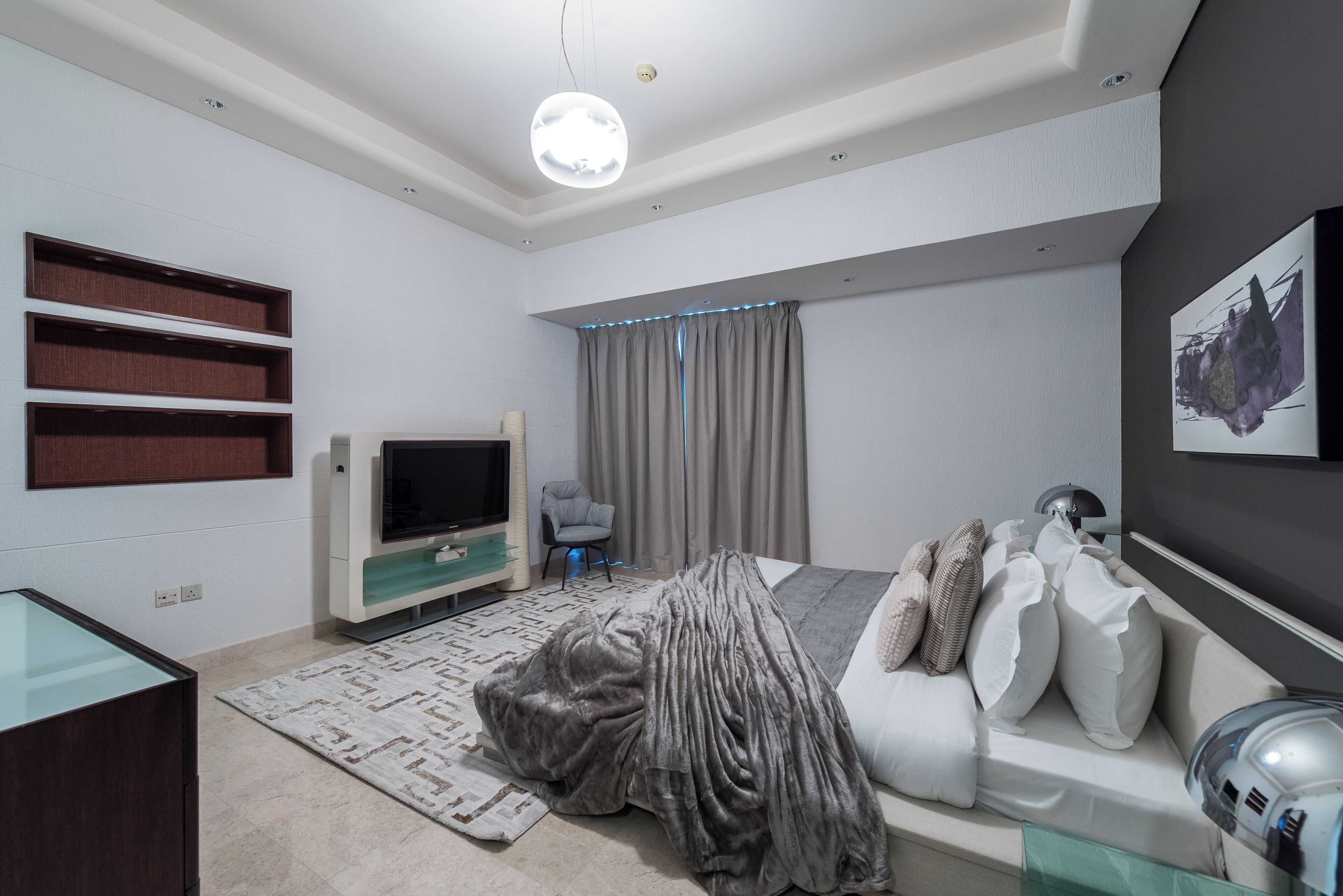 A modern bedroom with a bed, a TV, and built-in shelves.