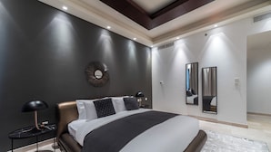 A modern bedroom with a large bed, a round mirror, and a nightstand with a lamp. - EDEN'S Homes & Villas - KG tower (Dubai)