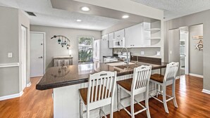 Una cocina con una isla central, taburetes de bar, microondas y estufa.