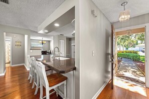 A modern kitchen with a central island, white bar stools, and a dining area. - Your Slice of Paradise Near Siesta Key (Sarasota)