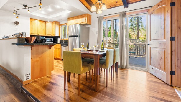 A modern kitchen with wooden cabinets, a stainless steel refrigerator, and a dining area with a wooden table and chairs. - Steps to Trails & Minutes to Heavenly + Firepit | Bluewood Cabin by AvantStay (South Lake Tahoe)