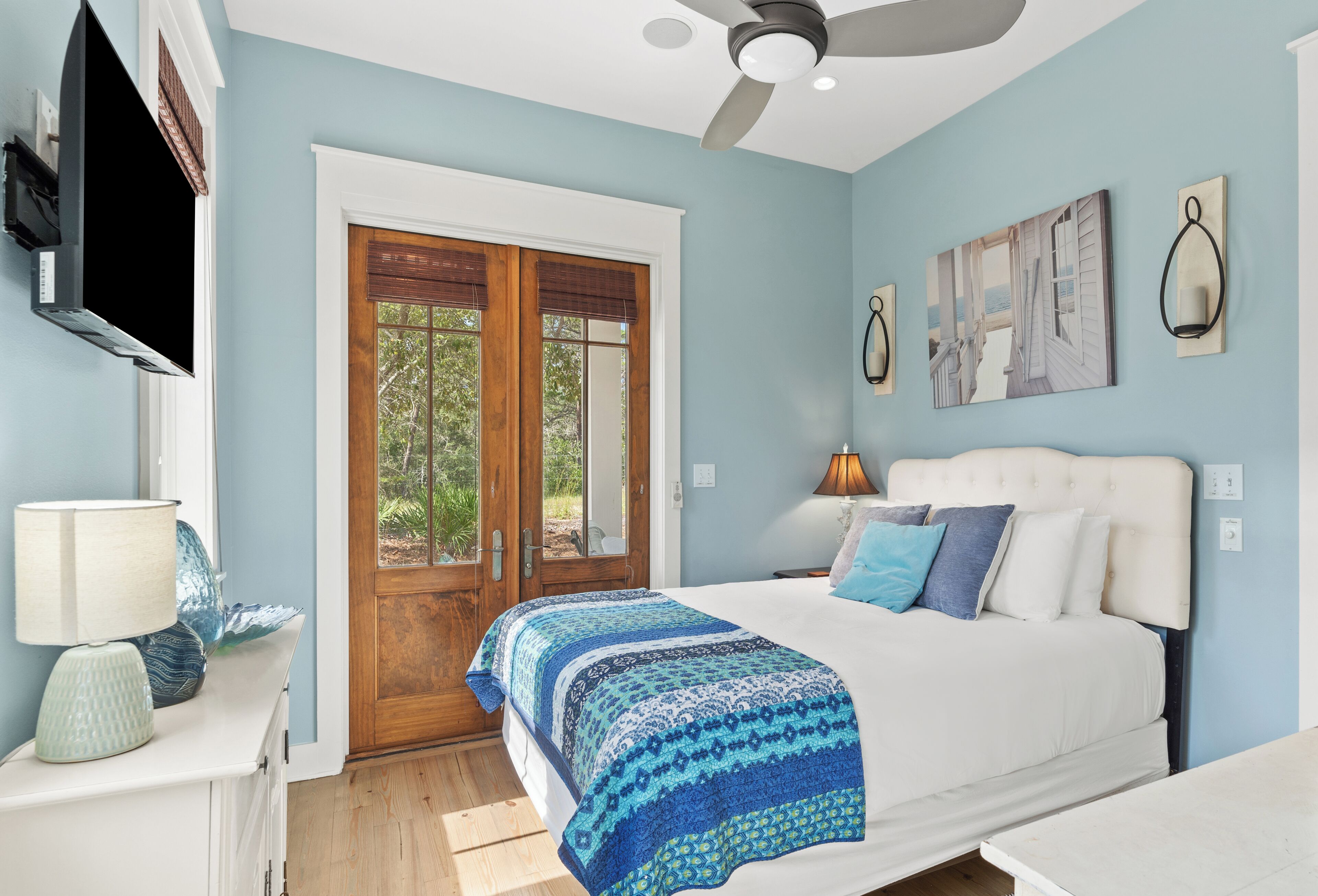 A bedroom with a bed, a TV, a door, and a ceiling fan.