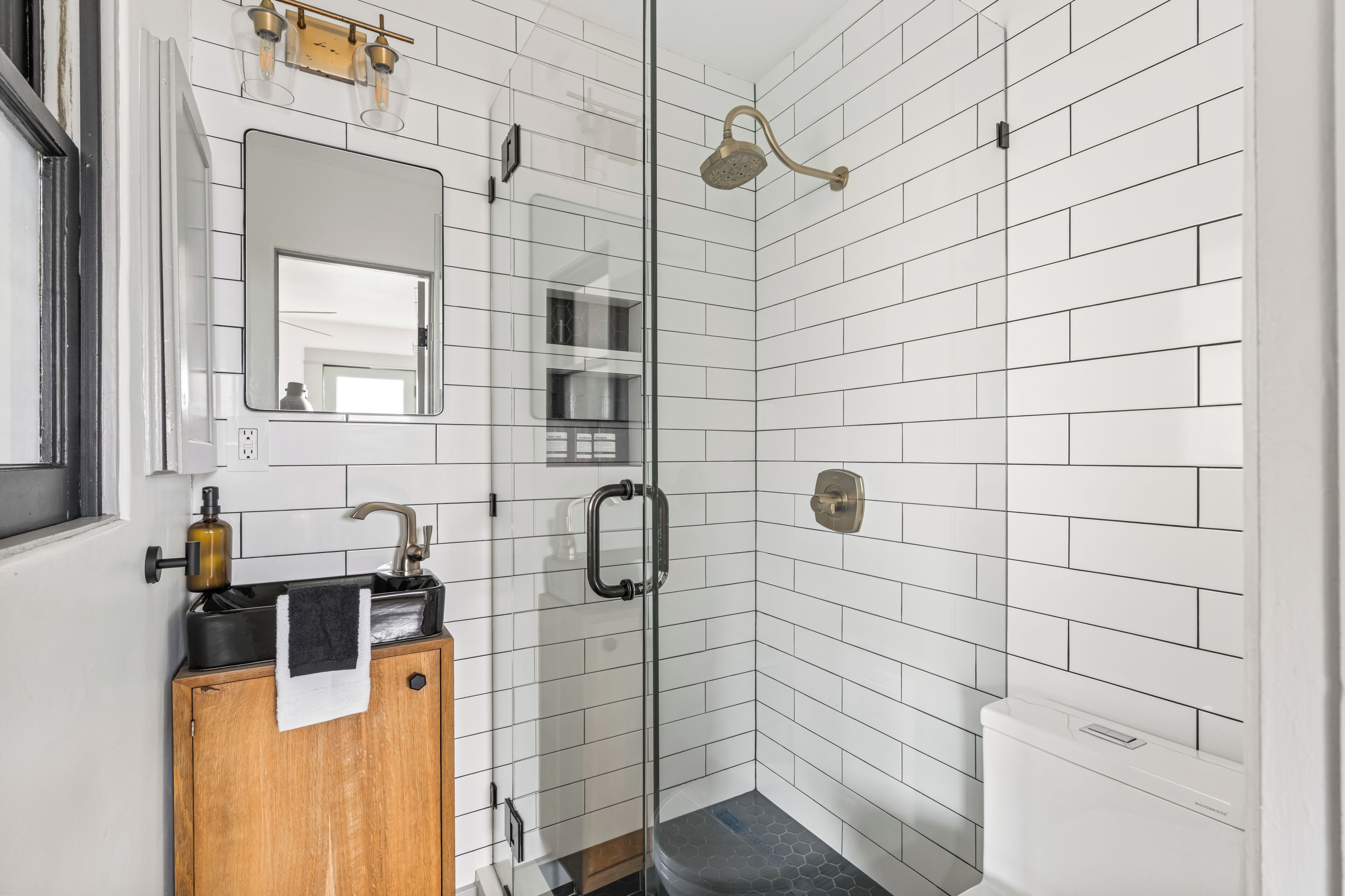 A modern bathroom with white subway tiles, a glass shower enclosure, a wooden cabinet with a towel, and a toilet.