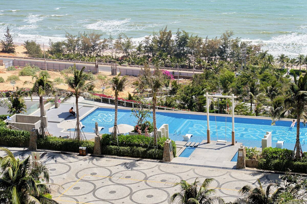 A pool area with a view of the ocean, surrounded by palm trees and a sandy beach.