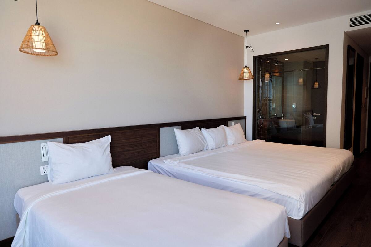 A hotel room with two beds, a wooden headboard, and a glass shower enclosure.