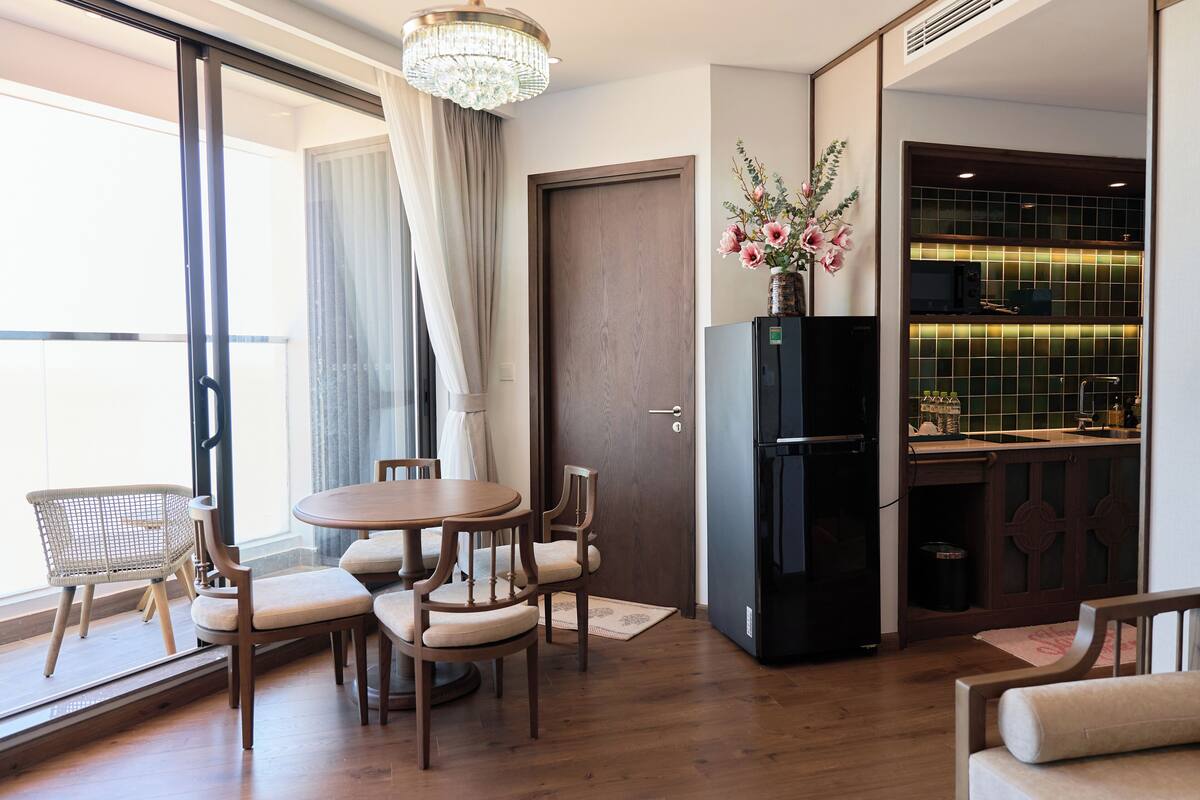 A modern hotel room with a dining area, a kitchen, and a large window.