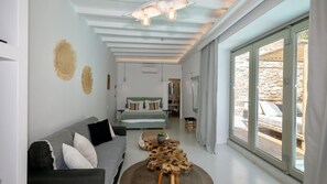 A modern bedroom with a bed, a sofa, a wooden coffee table, and a view through a glass door.