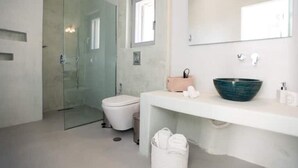 Une salle de bain moderne avec une douche à parois de verre, des toilettes blanches et un grand miroir au-dessus d’un lavabo blanc doté d’une cuvette bleue.