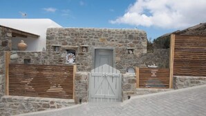 Un bâtiment en pierre doté d’un portail et d’une porte en bois, entouré d’un mur en pierre et d’une zone pavée.