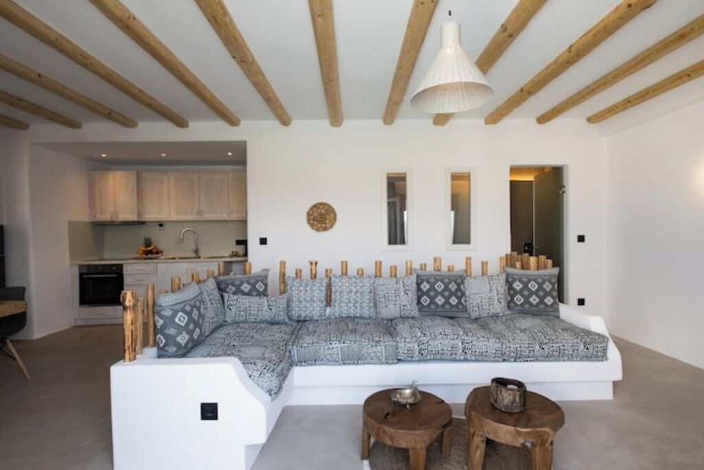 Un salon moderne avec un grand canapé d’angle, des poutres en bois au plafond et une cuisine en arrière-plan.