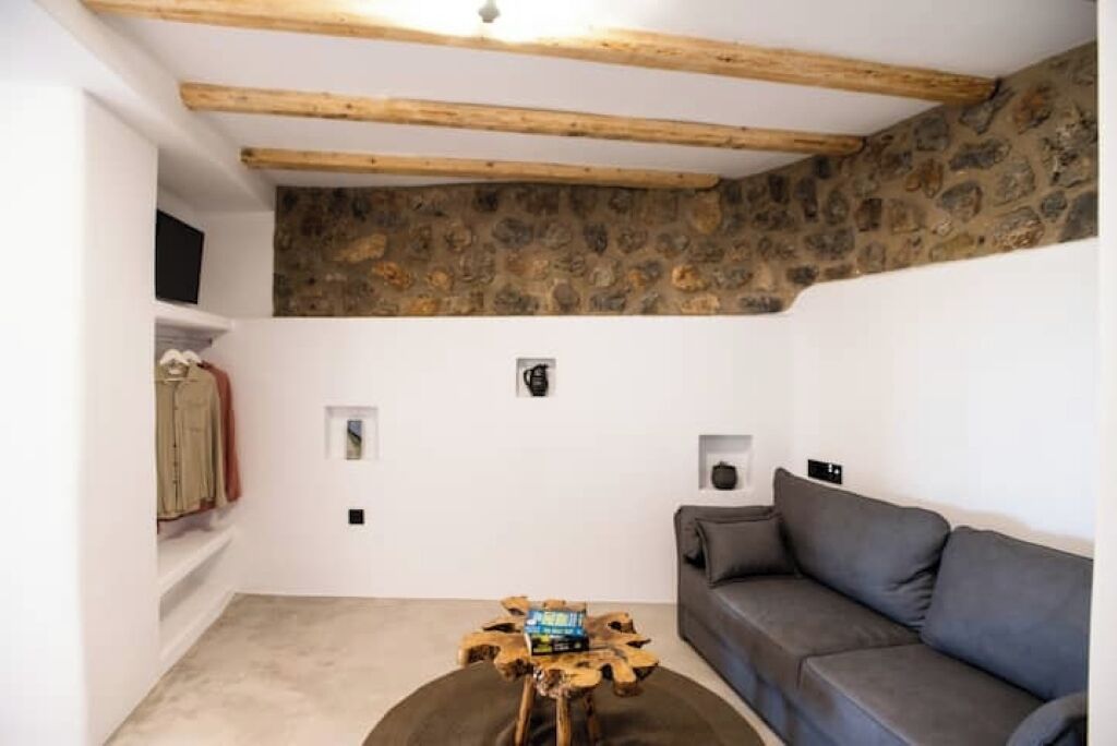A cozy living room with a stone wall, a grey sofa, a wooden coffee table, and a television on the left.