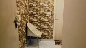 A narrow hallway with a stone wall, a white chair, and a door at the end. - Roomshala Hotel Mannat (New Delhi)