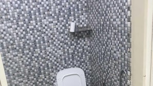 A small bathroom with a tiled floor, a toilet, a sink, and a trash bin. - Roomshala Hotel Mannat (New Delhi)