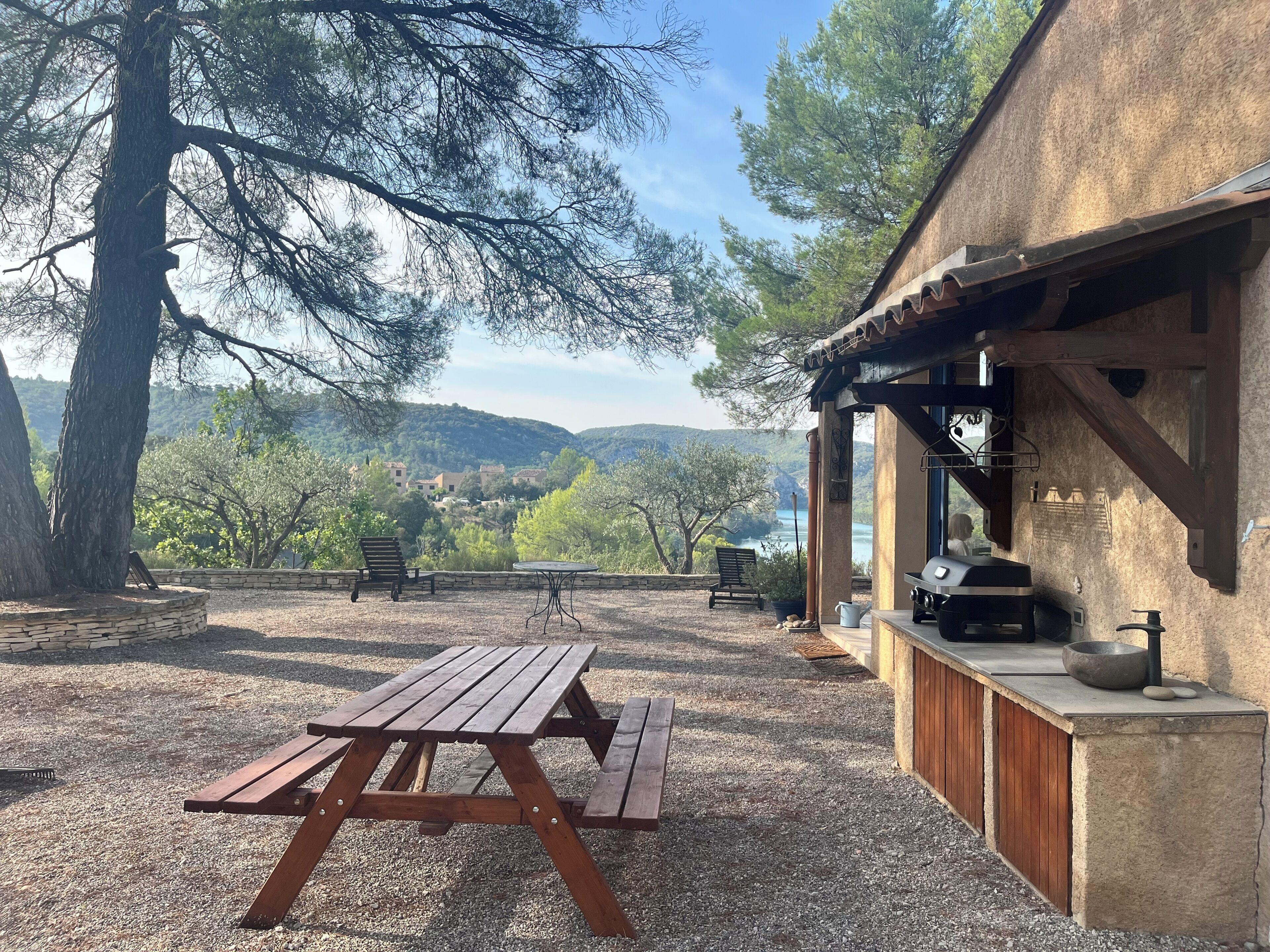 Une terrasse extérieure avec une table et des bancs en bois, offrant une vue sur un paysage pittoresque composé de collines et d’arbres.