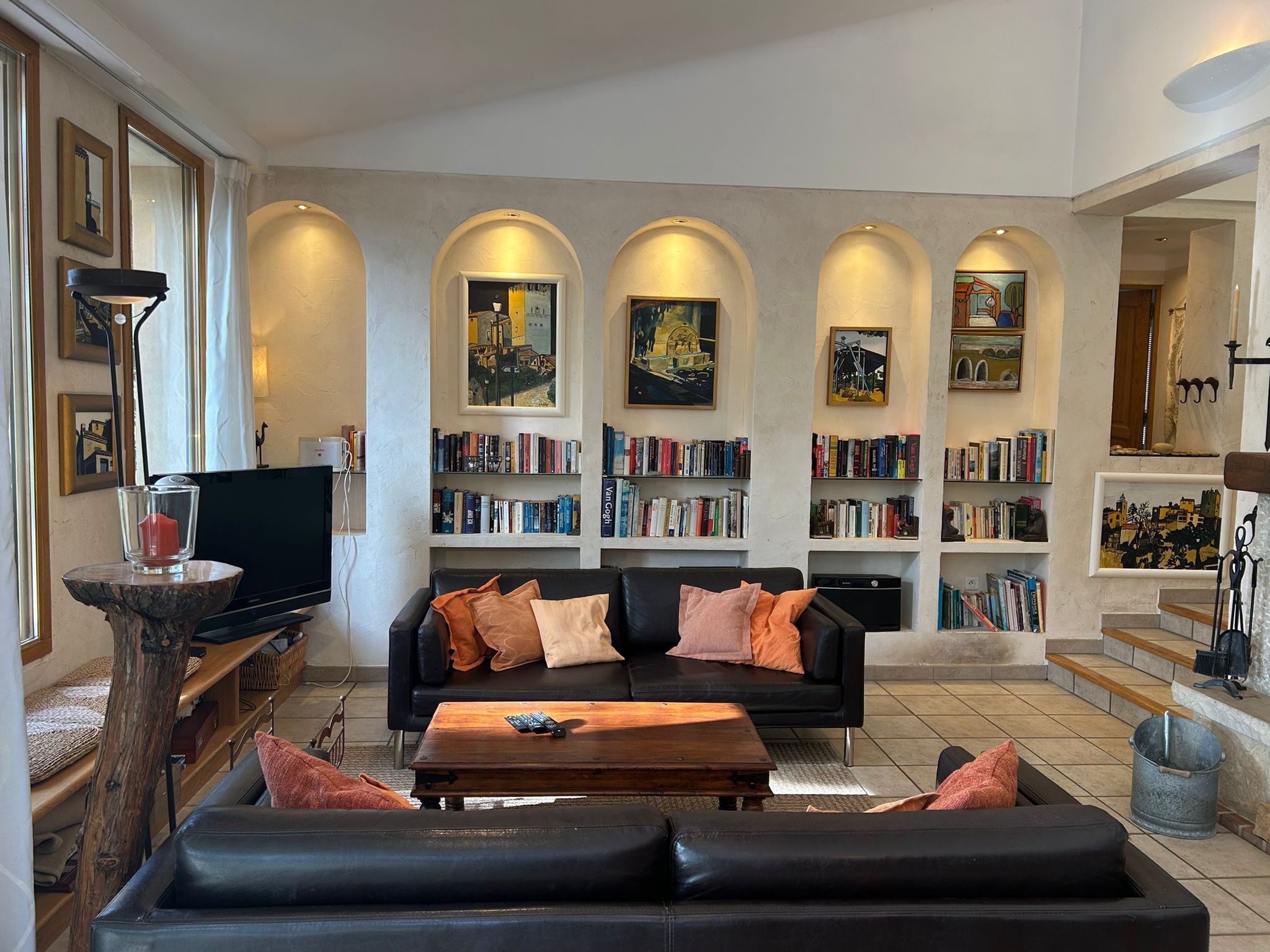 A spacious living room with a black leather sofa, a wooden coffee table, and a bookshelf filled with books.