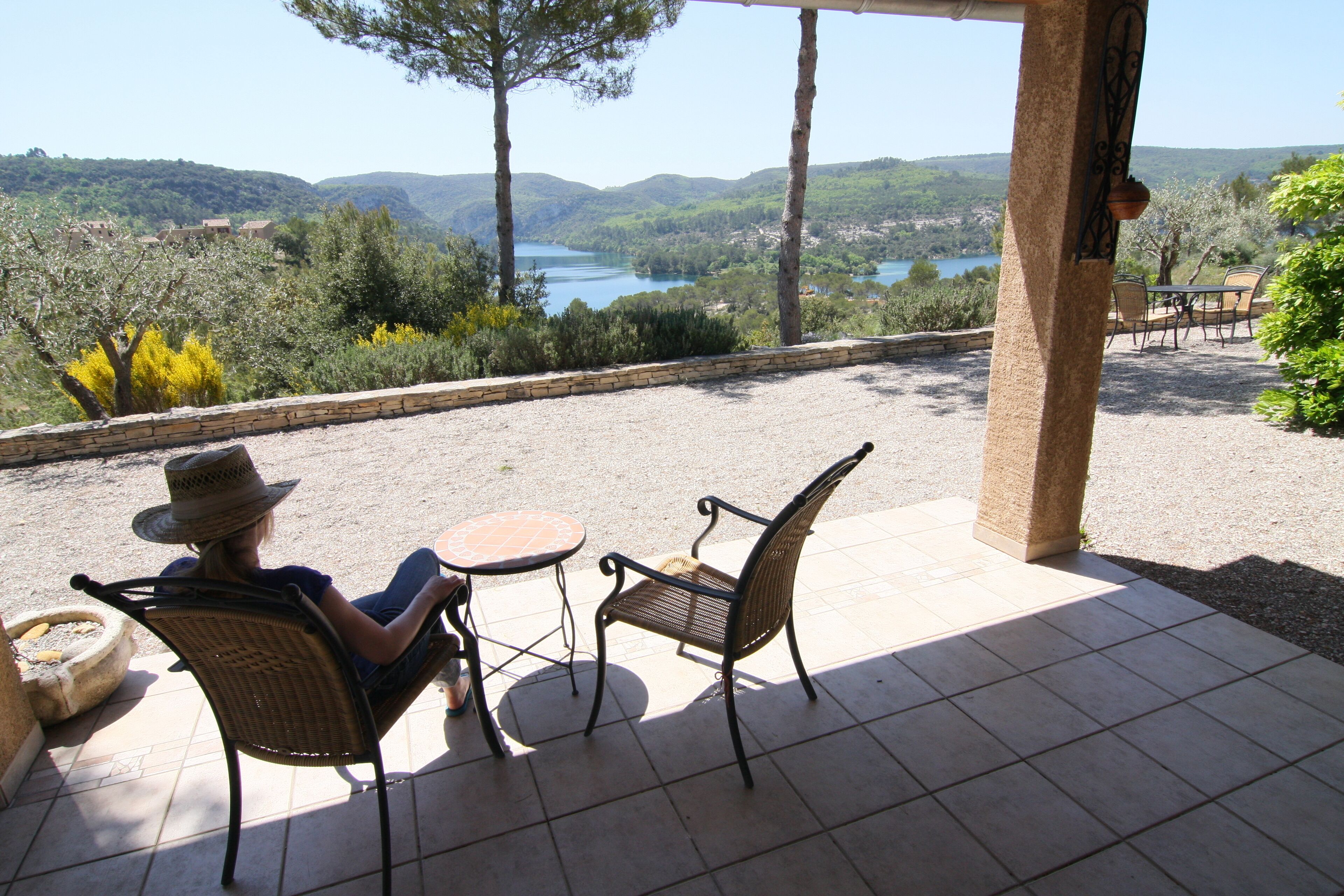 Un patio con dos sillas de mimbre y una mesa, con vistas a un paisaje pintoresco con colinas y un lago.