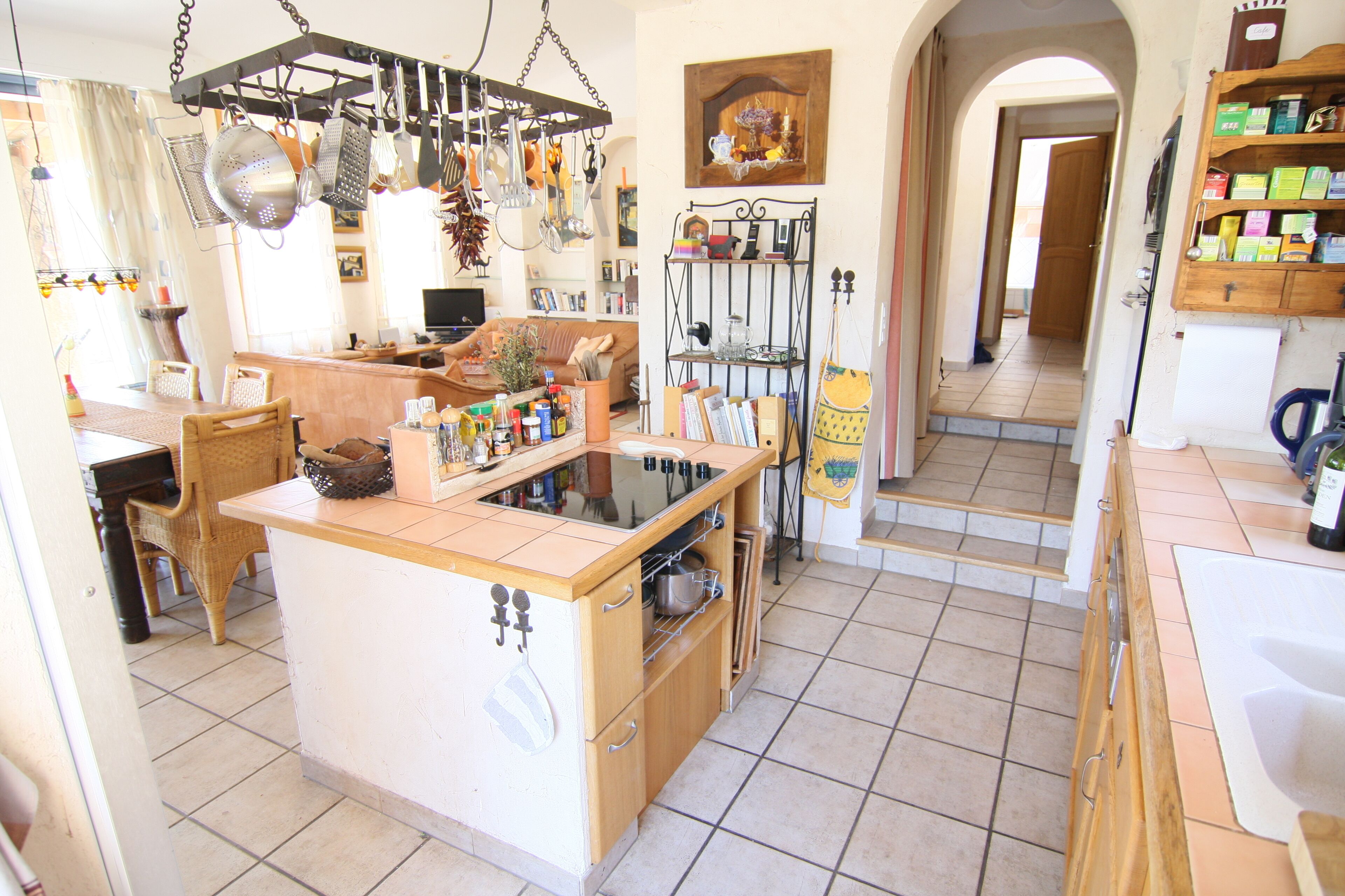 A kitchen with a central island, wooden cabinets, and various kitchen utensils hanging above.