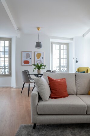 A modern living room with a sofa, a dining table with chairs, and a potted plant.