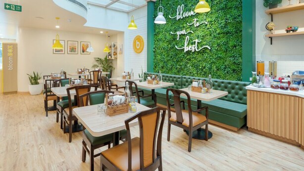 A restaurant with a green wall, wooden tables, and yellow pendant lights. - Bloom Hotel - M Block GK2 (New Delhi)