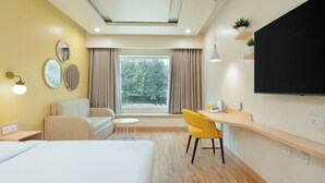 A modern hotel room with a bed, a desk, a chair, a TV, and a window with curtains. - Bloom Hotel - M Block GK2 (New Delhi)