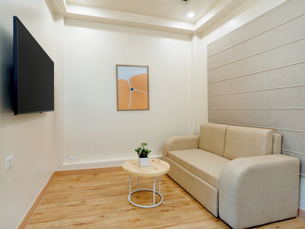Una sala de estar moderna con un sofá, una mesita redonda con una planta y un televisor de pantalla plana montado en la pared.