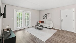 A living room with a white sofa, a coffee table, and a TV mounted on the wall.