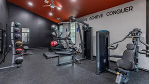 Una palestra con diverse attrezzature per esercizi, una ventola a soffitto e scritte motivazionali sulla parete.