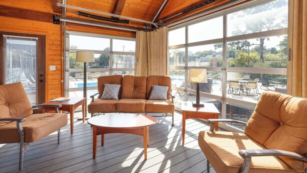 Un terrazzo in legno con divano, poltrone e tavolo, affacciato su una piscina e un'area relax all'aperto.